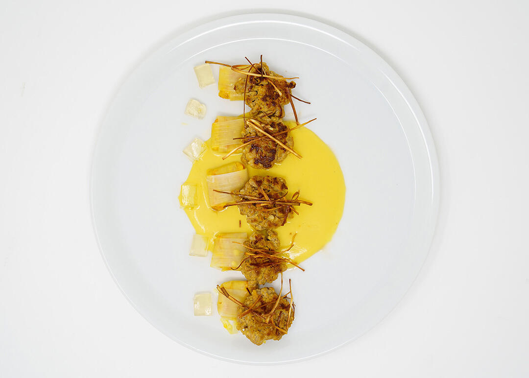 Plato gourmet con salsa amarilla de azafrán sobre fondo blanco.